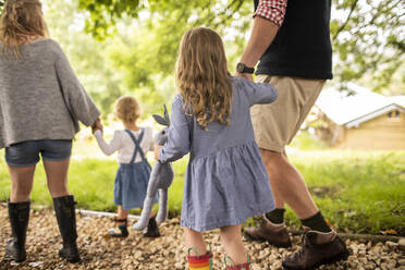 Cute girl with stuffed animal holding hands with father on path - CAIF30359