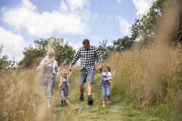 Happy family holding hands running in sunny rural field - CAIF30361