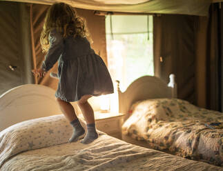 Glückliches Mädchen im Kleid springt auf dem Bett in der Kabine - CAIF30369