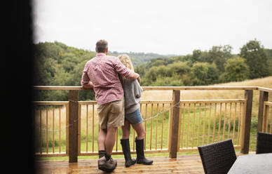 Affectionate couple hugging on cabin balcony overlooking trees - CAIF30381