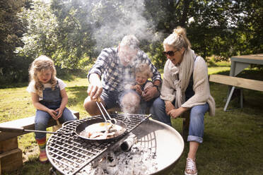 Happy family cooking breakfast on campsite grill - CAIF30386
