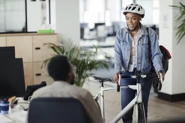 Geschäftsfrau mit Helm und Fahrrad im Gespräch mit Mitarbeiterin im Büro - CAIF30402