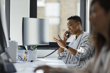 Businesswoman talking on telephone at computer in office window - CAIF30417