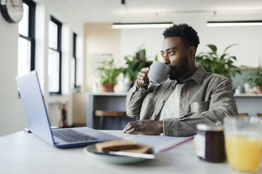 Geschäftsmann trinkt Kaffee am Laptop im morgendlichen Büro - CAIF30418