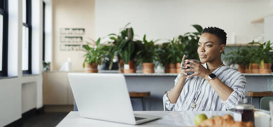 Junge Geschäftsfrau mit Kaffee am Laptop im Büro - CAIF30422