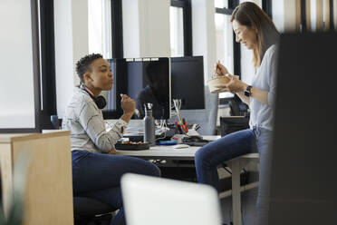 Businesswomen eating takeout lunch at desk in office - CAIF30426