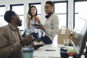 Business people eating takeout lunch at desk in office meeting - CAIF30449