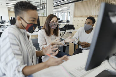 Business people in face masks video conferencing at office computer - CAIF30460
