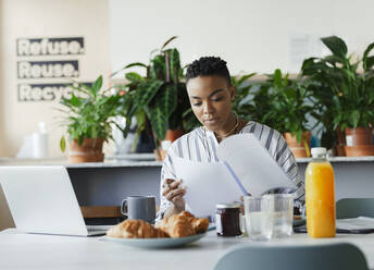 Businesswoman reviewing paperwork at breakfast in office lounge - CAIF30462