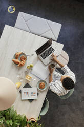 Businesswoman working at laptop on table with breakfast - CAIF30465