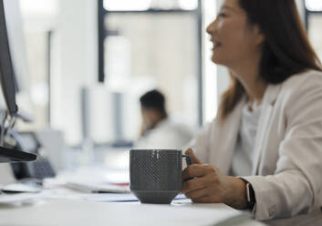 Businesswoman drinking coffee at computer in office - CAIF30471