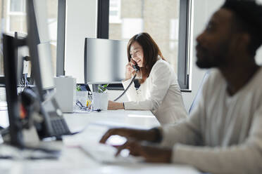 Businesswoman talking on telephone at sunny office window - CAIF30474