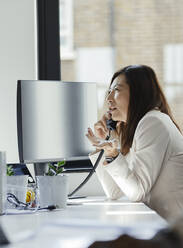 Businesswoman talking on telephone at office window - CAIF30477