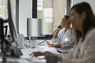 Businesswoman talking on telephone at computer in office window - CAIF30479