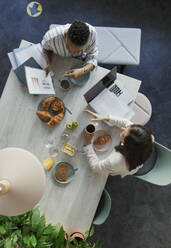 Businesswomen discussing paperwork at breakfast meeting in office - CAIF30480