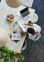 Businesswoman reviewing paperwork at breakfast in office - CAIF30482