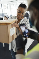 Businesswoman receiving packages from courier with smart phone - CAIF30487