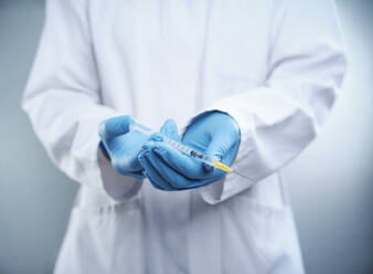 Female doctor wearing lab coat and protective glove holding COVID-19 vaccine syringe - DIKF00589