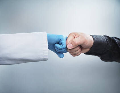 Weibliche Mitarbeiterin im Gesundheitswesen gibt einem männlichen Patienten einen Faustschlag vor weißem Hintergrund - DIKF00591