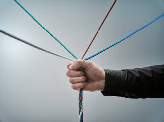 Mature man holding colorful tangled cables over white background - DIKF00593