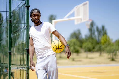 Mann hält Basketball, während er auf einem Sportplatz an einem sonnigen Tag steht - OCMF02119