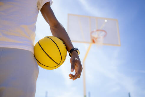 Man holding basketball while standing at sports court - OCMF02122