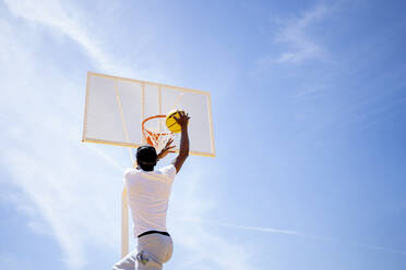 Junger Mann spielt Basketball auf einem Sportplatz an einem sonnigen Tag - OCMF02123