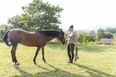 Frau sieht Pferd an, während sie auf einer Wiese steht - WPEF04585