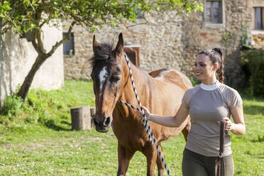 Smiling woman holding rope while walking by horse during sunny day - WPEF04588