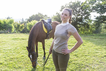 Smiling woman holding rein while standing by horse at ranch - WPEF04604