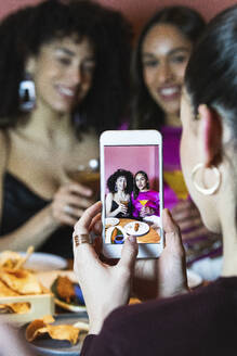 Frau fotografiert ihre Freunde mit dem Smartphone im Restaurant - PNAF01708