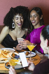 Freundinnen lächelnd bei der Benutzung von Handys am Esstisch - PNAF01709