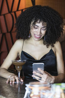 Lächelnde Frau, die ein Mobiltelefon bei einem Getränk im Restaurant benutzt - PNAF01711