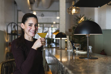 Lächelnde Frau hält ein Martini-Glas, während sie im Restaurant sitzt - PNAF01719