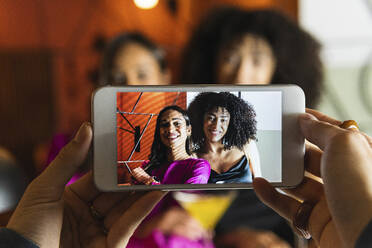 Woman photographing friends through smart phone at restaurant - PNAF01736