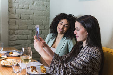 Geschäftsfrau, die ein Selfie mit dem Smartphone eines Kollegen im Restaurant macht - PNAF01753