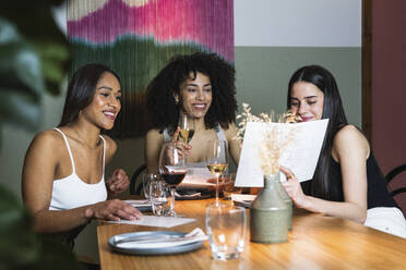 Frau zeigt Freunden die Speisekarte, während sie in einem Restaurant etwas trinkt - PNAF01758