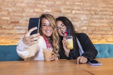 Lächelnde Frau, die ein Selfie mit ihrer Freundin über ihr Smartphone in einer Bar macht - JRVF00882