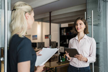 Junge Geschäftsfrau bespricht sich mit einer Kollegin, während sie an der Tür im Büro steht - DIGF15306