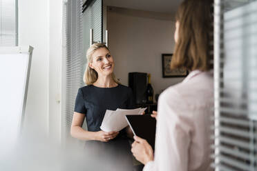 Lächelnde Unternehmerin, die eine Kollegin anschaut, während sie an der Tür im Büro diskutiert - DIGF15307
