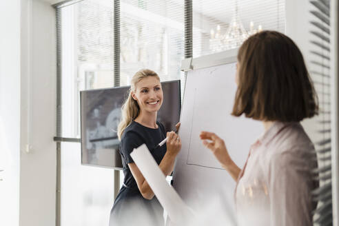 Lächelnde weibliche Fachkraft, die einen Mitarbeiter ansieht, während sie an einem weißen Brett im Büro steht - DIGF15308