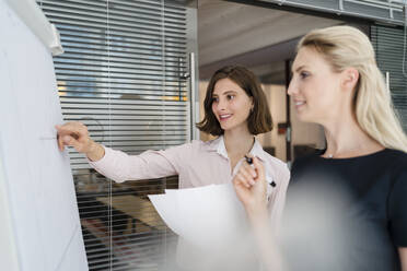 Young businesswomen discussing over white board during meeting in office - DIGF15309