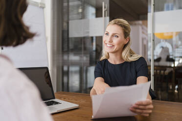 Glückliche schöne Unternehmerin, die mit einer Kollegin im Büro über ein Dokument diskutiert - DIGF15319