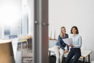 Happy young businesswoman discussing over document while sitting on desk in office - DIGF15332