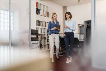 Female entrepreneurs discussing over digital tablet while walking in office - DIGF15342