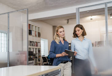 Young female professional discussing over digital tablet with colleague in office - DIGF15343