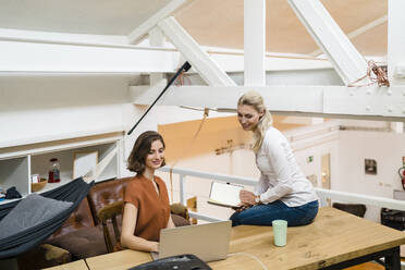 Lächelnde junge Geschäftsfrauen, die über einem Laptop in einem kreativen Büro diskutieren - DIGF15358