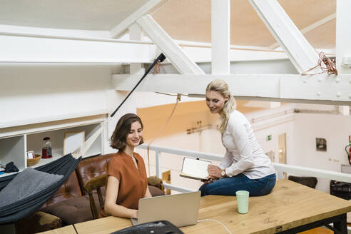 Smiling young businesswomen discussing over laptop in creative office - DIGF15358