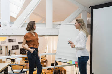 Young businesswomen discussing over white board while planning strategy in creative office - DIGF15370