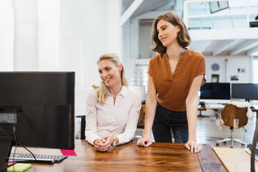 Unternehmerinnen schauen auf den Computer, während sie in einem kreativen Büro zusammenarbeiten - DIGF15373